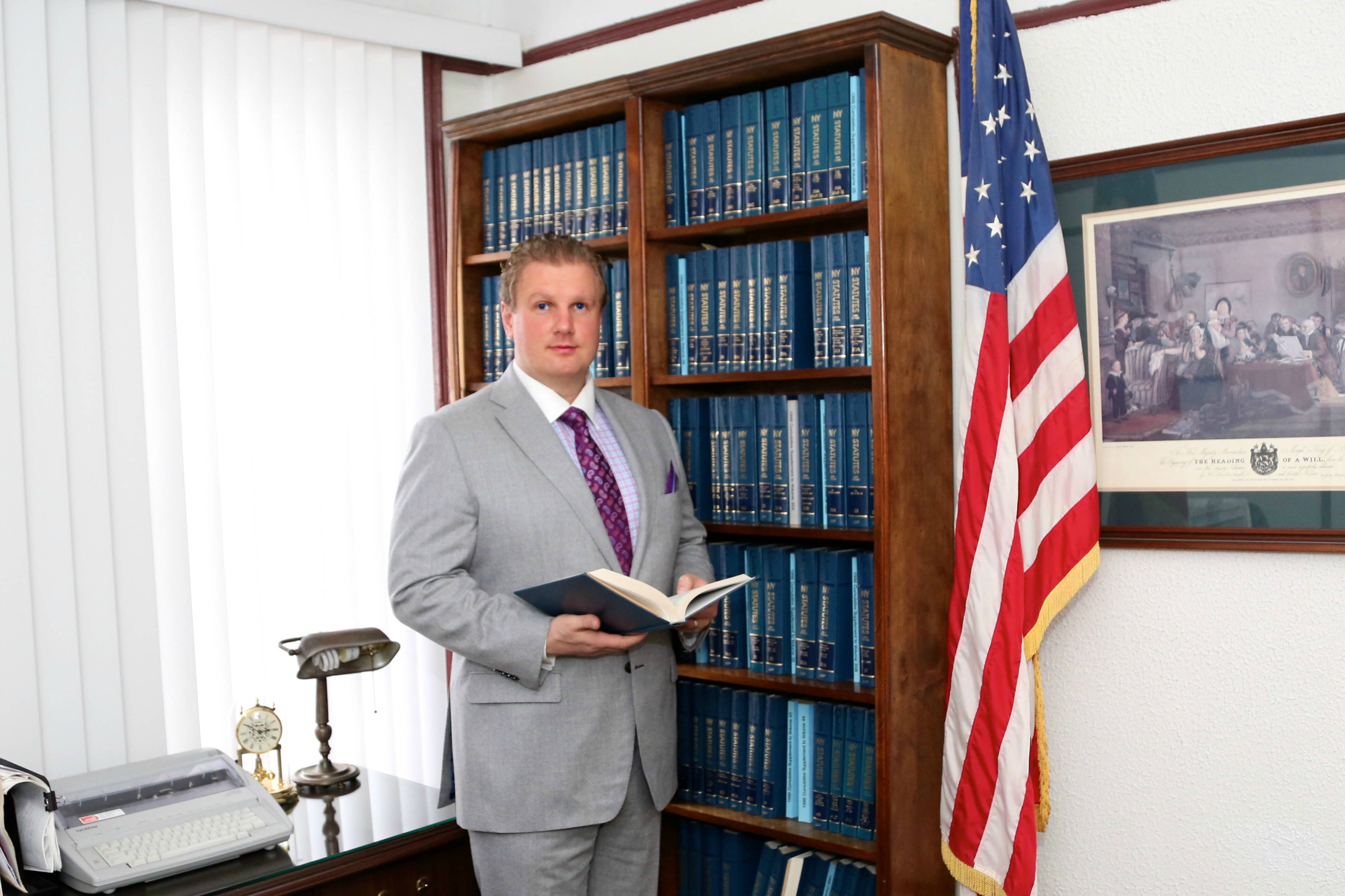 Michael L. Walker holding an open book in his law library beside an American flag